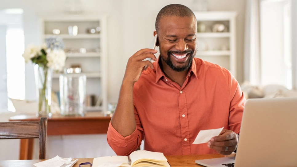 Mature African man sitting behind his desk smiling when receiving a quote on the phone.
