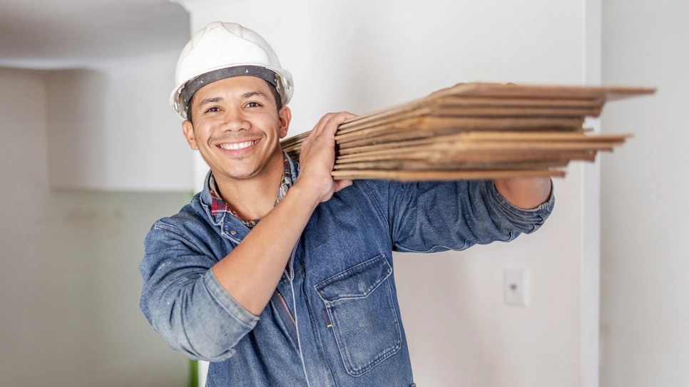 Smiling construction worker holding wood for maintenance.