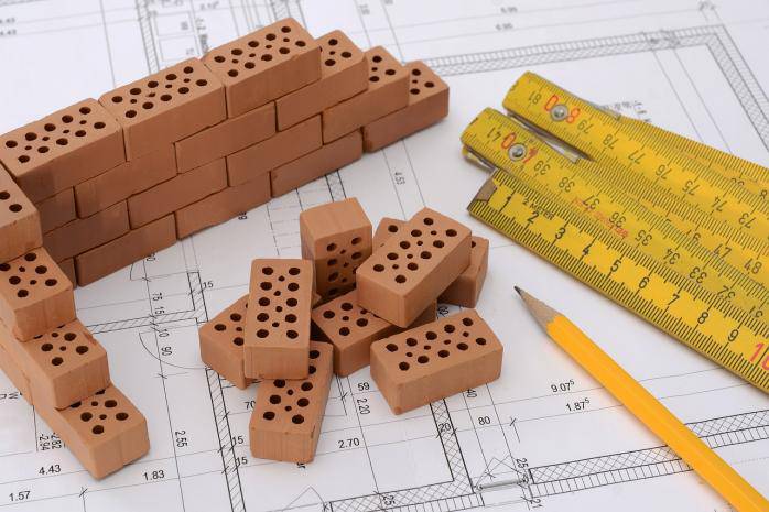Building plan with a pencil and miniature bricks on it.