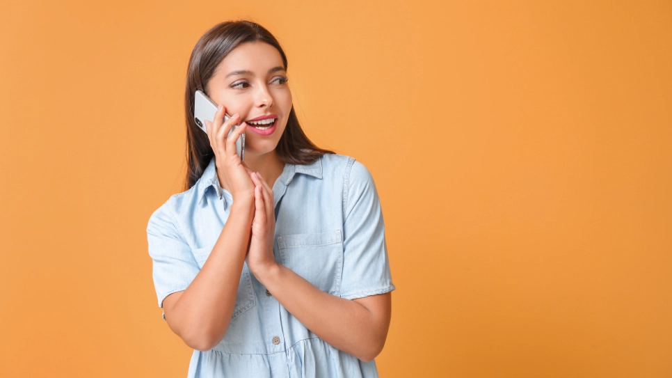 A woman talking on a mobile phone. Orange background.