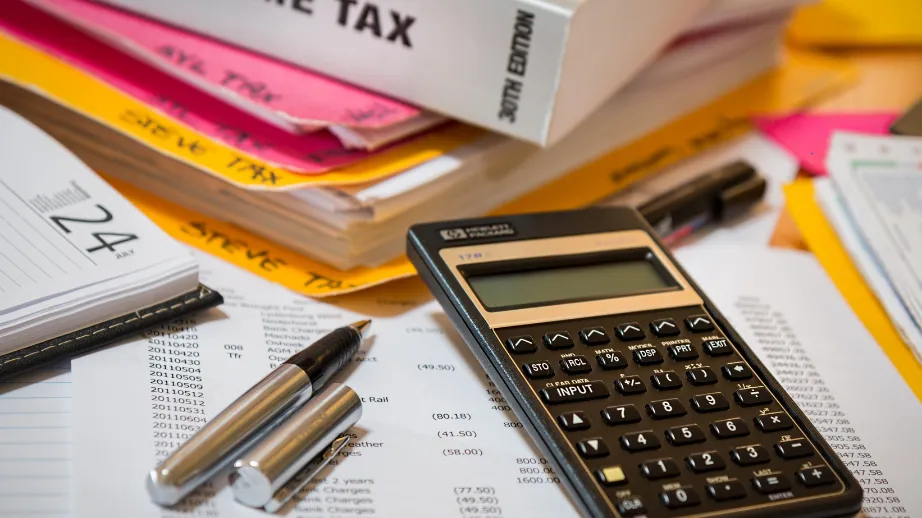Calculator, pen, and financial documents on a desk with files labelled ‘Income Tax’.