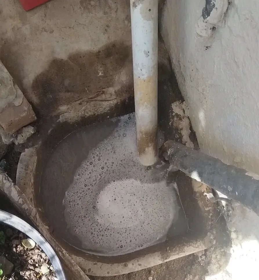 Outdoor drain with standing water and soap suds indicating a possible clogging issue.