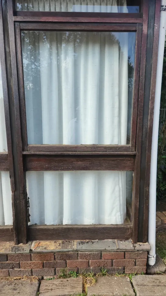 A wooden window frame showing signs of rot and decay, with peeling paint and damaged wood.