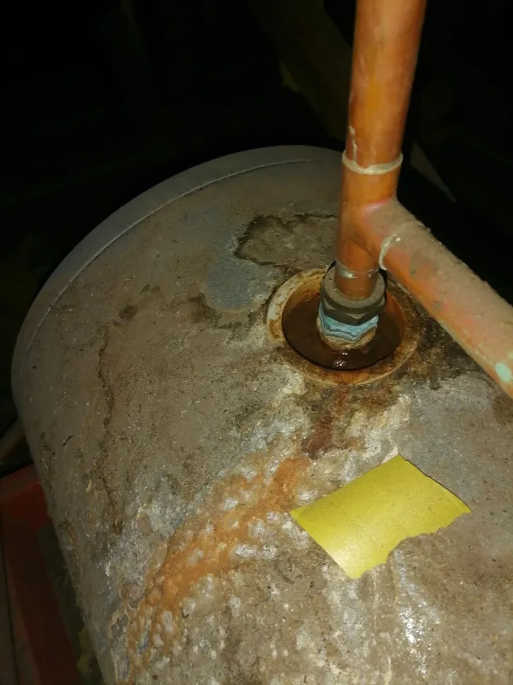 Corroded water heater tank with visible rust and leakage around pipe connection, indicating damage.