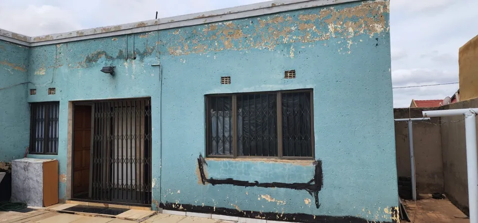 Blue house with peeling exterior paint, revealing patches of bare wall, indicating potential water damage.