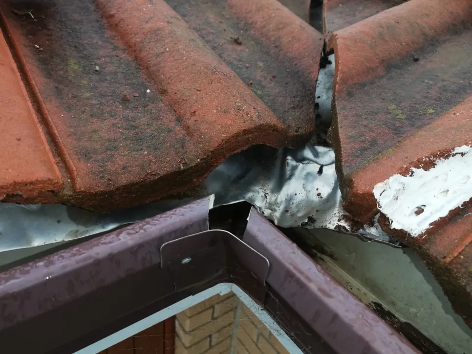 Broken roof tiles with damaged flashing causing potential leaks.