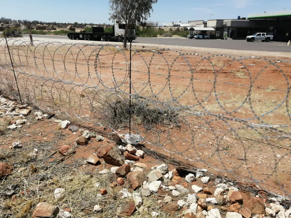 Barbed wire fence securing a perimeter in a rural area with rocky terrain and sparse vegetation.