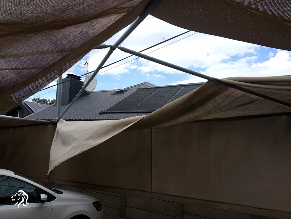 Torn fabric on outdoor shade structure with visible roof and sky, highlighting potential weather damage.
