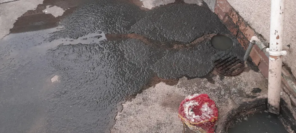 Overflowing outdoor drain with accumulated water and debris indicating a blockage issue.
