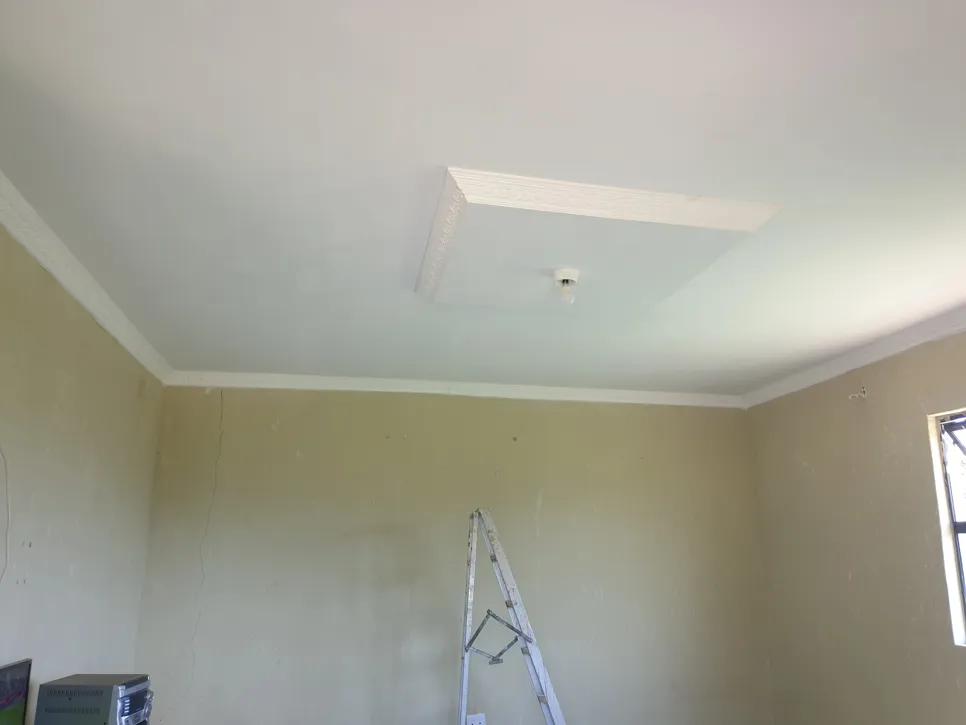 Living room with visible ceiling crack and ladder against beige wall, indicating structural issues.