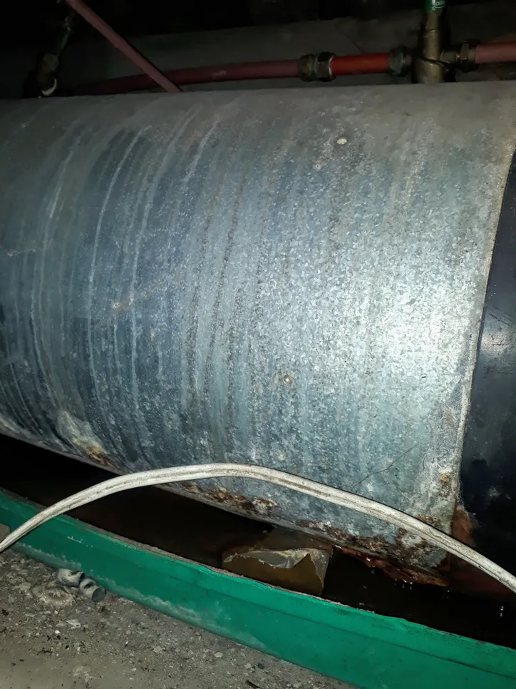 Corroded water heater tank with visible rust and leakage, indicating potential failure and need for replacement.