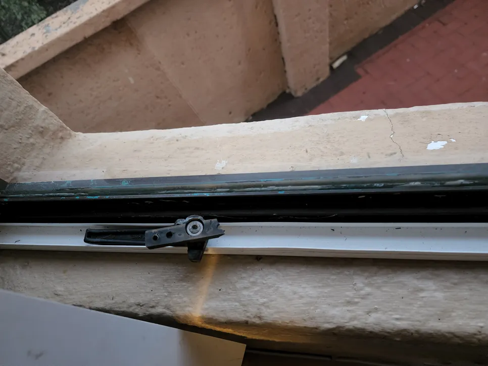 Close-up of a broken window latch mechanism on a window frame, highlighting the need for repair or replacement.
