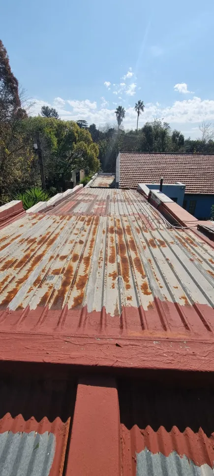 Corrugated metal roof with visible rust and partial red paint, set against a clear blue sky.