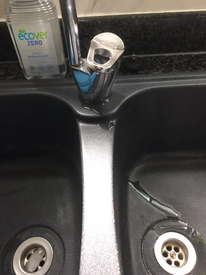 A cracked kitchen sink with visible water leakage around the faucet area, indicating potential plumbing issues.