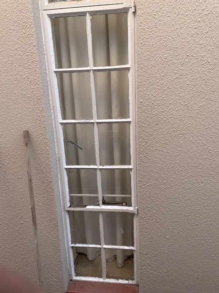 A tall, narrow wooden window frame with peeling white paint against a textured wall.