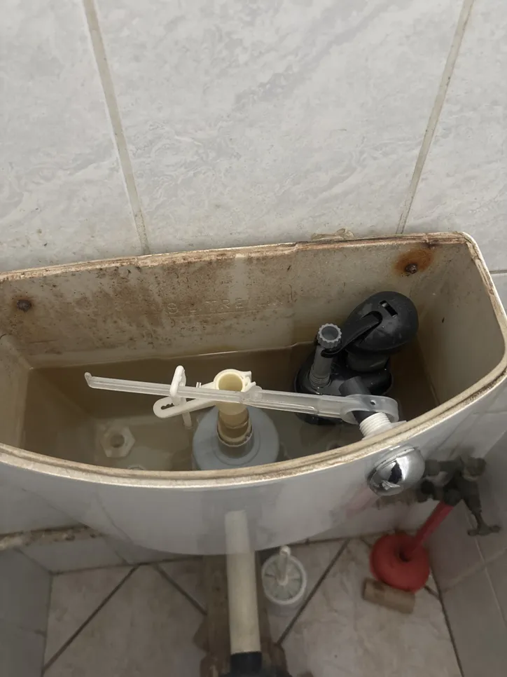 Open toilet tank showing a malfunctioning fill valve and rusty components.