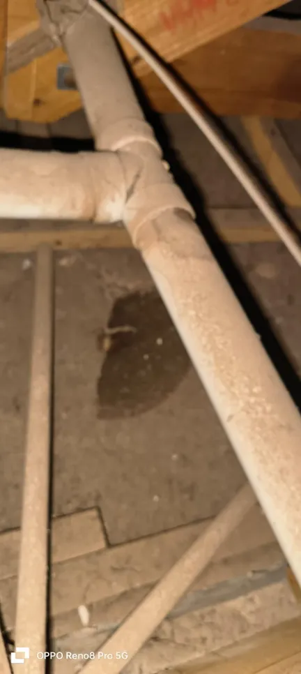Dusty pipes with a visible leak in an attic space, indicating potential water damage.