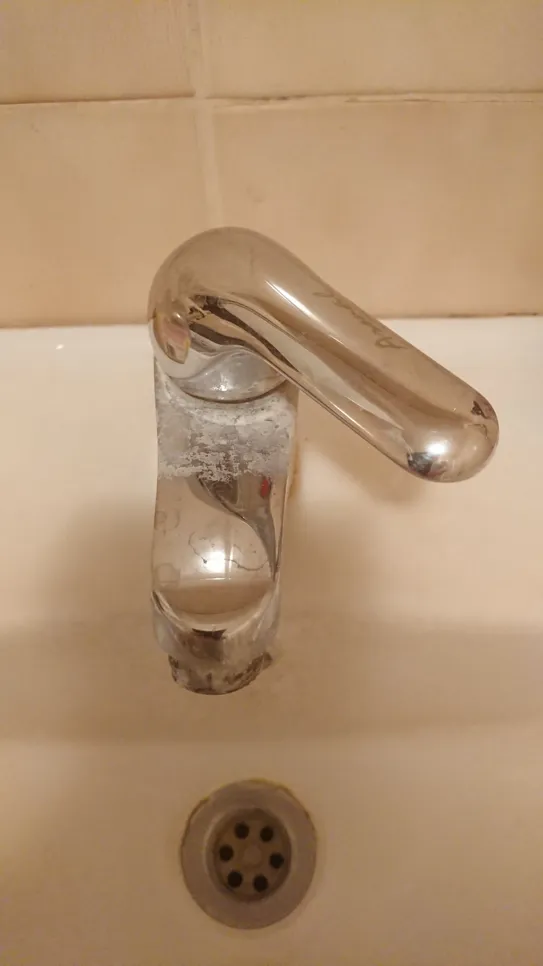 Close-up of a bathroom faucet with visible limescale buildup, highlighting mineral deposits and cleanliness issues.