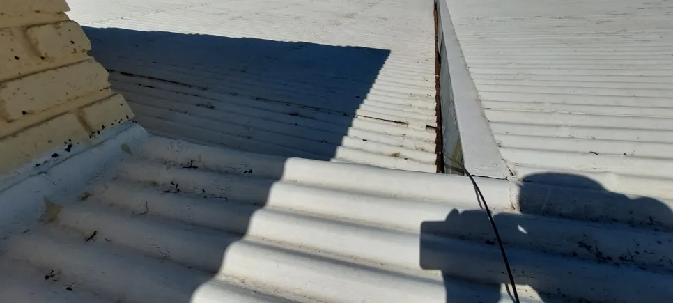Corrugated metal roof showing a seam and potential water leakage point near a chimney.