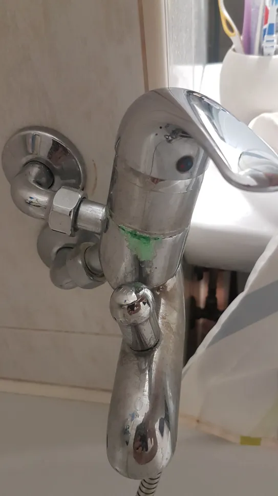 Corroded bathroom faucet showing green discoloration and mineral buildup around the joint.