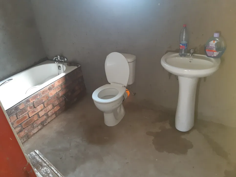 Concrete bathroom with water leakage near toilet and sink, causing damp floors and potential damage.