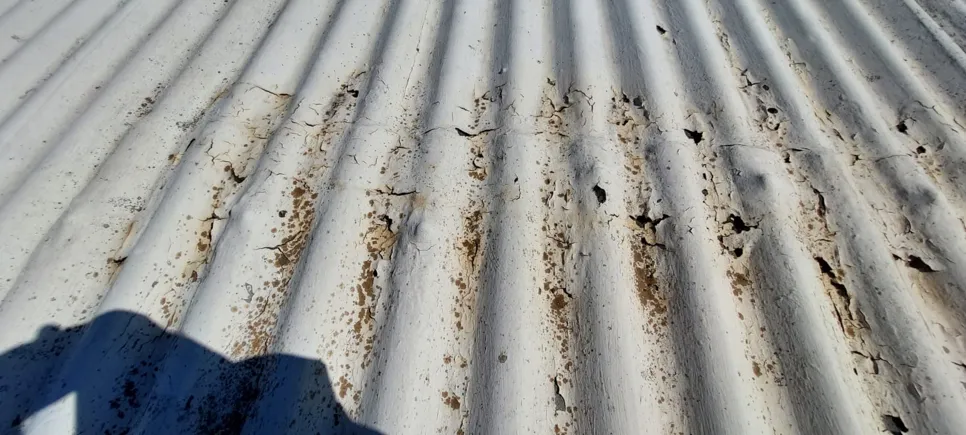 Close-up of a corroded corrugated metal roof with visible rust and deterioration.