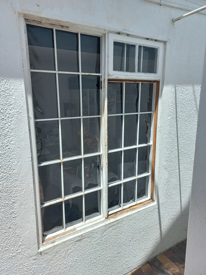 Exterior window frame with peeling white paint and visible wood damage, indicating weather exposure.