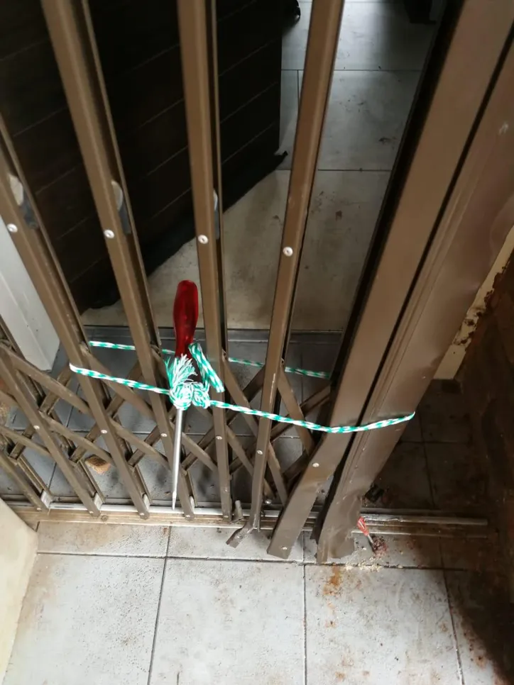 Improvised lock on sliding gate using rope and screwdriver, highlighting security concerns.