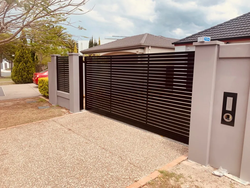 Sleek black horizontal slat driveway gate with electronic access control in a residential setting.