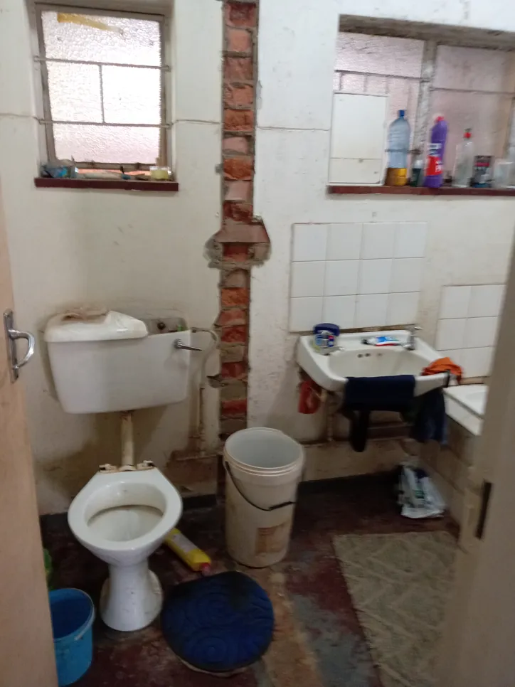 A bathroom with an exposed brick wall, showing a toilet, sink, and cleaning supplies.