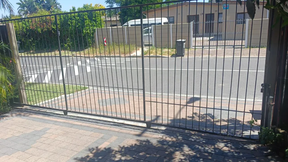 A metal sliding driveway gate with a paved entrance, facing a residential street.