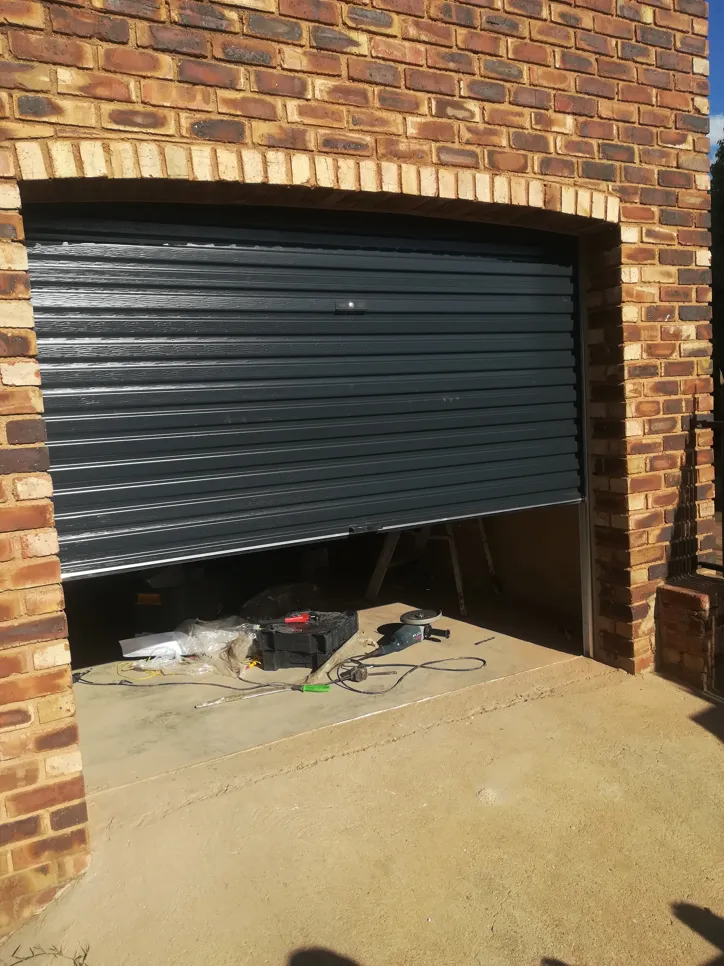 Partially open garage door showing misalignment and repair tools on the ground.