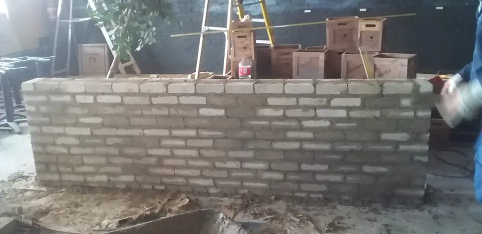 Partially constructed brick wall with mortar, surrounded by building materials and tools.