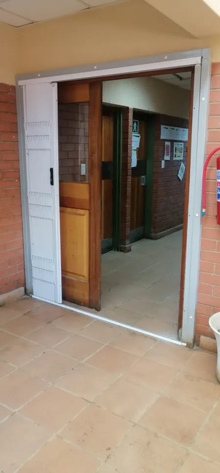 Open sliding security door in a hallway, revealing wooden interior doors and brick walls.