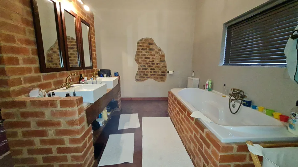 Rustic bathroom with exposed brick walls, dual sinks, and a bathtub, showcasing a warm, earthy aesthetic.