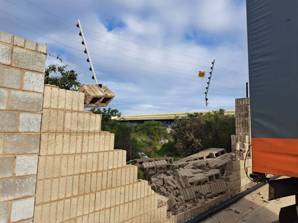 Damaged brick wall with fallen debris Collapsed brick wall section with scattered debris and visible electrical lines, indicating structural damage.