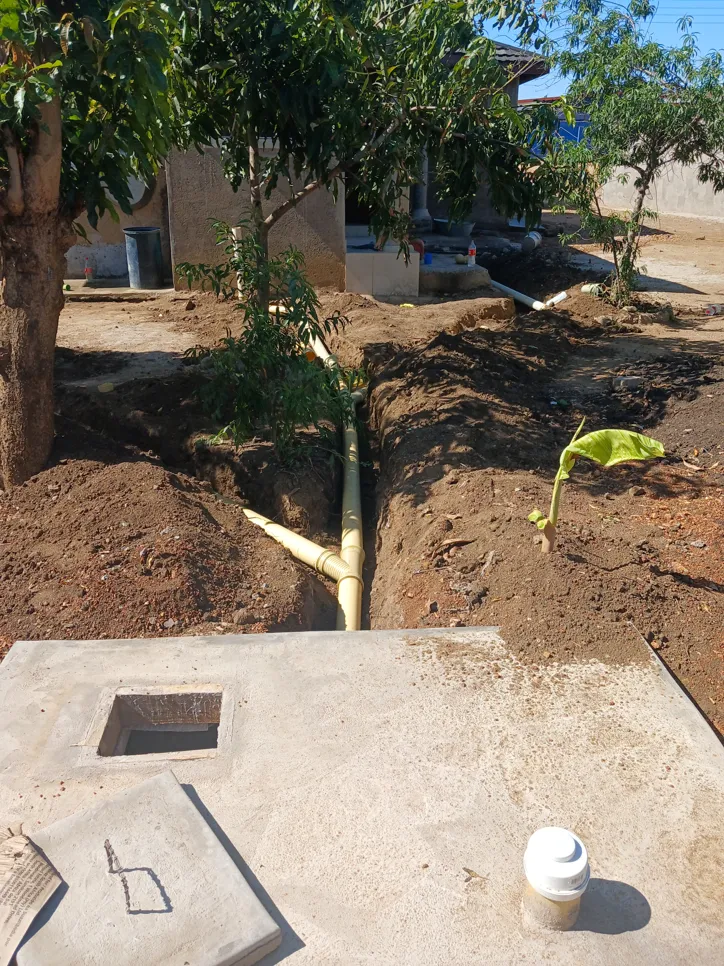 Newly installed underground drainage pipes in a garden area, surrounded by soil and trees.