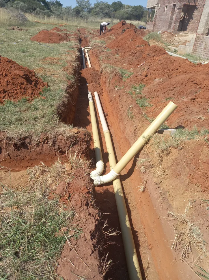 Trench with newly installed underground drainage pipes in a rural area, showcasing excavation and pipe placement.