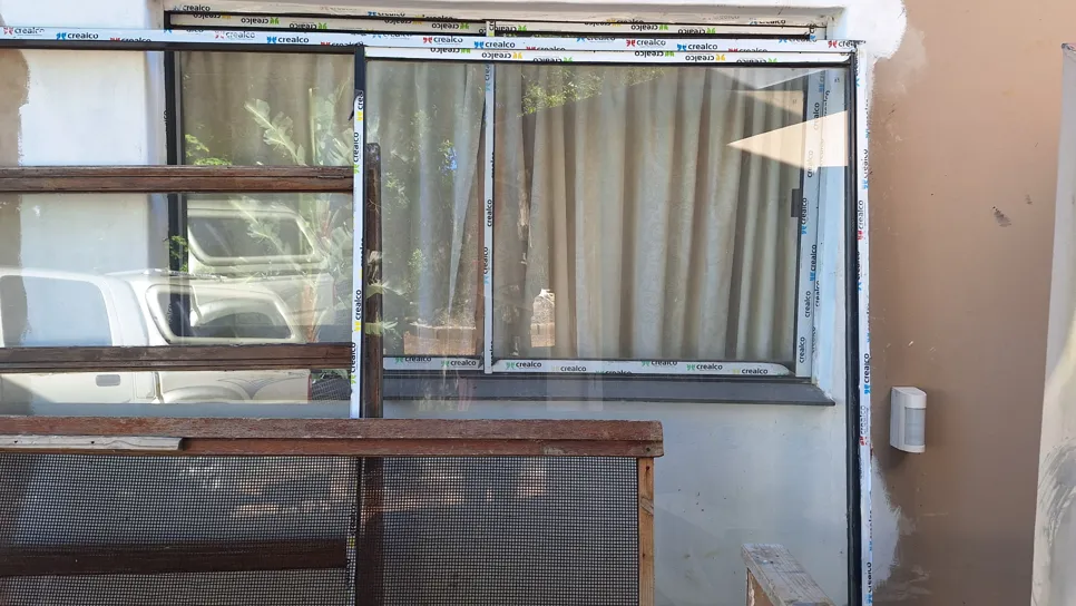 Partially installed window frame with visible protective tape in a residential setting.