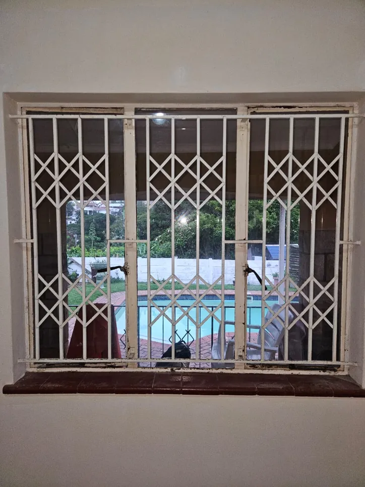 Window with metal security bars overlooking a backyard pool area, enhancing home safety.
