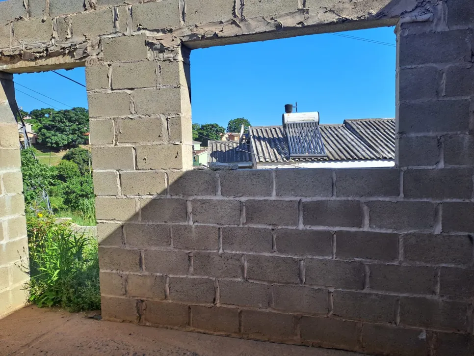 Unfinished brick wall with a window opening, overlooking a residential area with rooftops and greenery.
