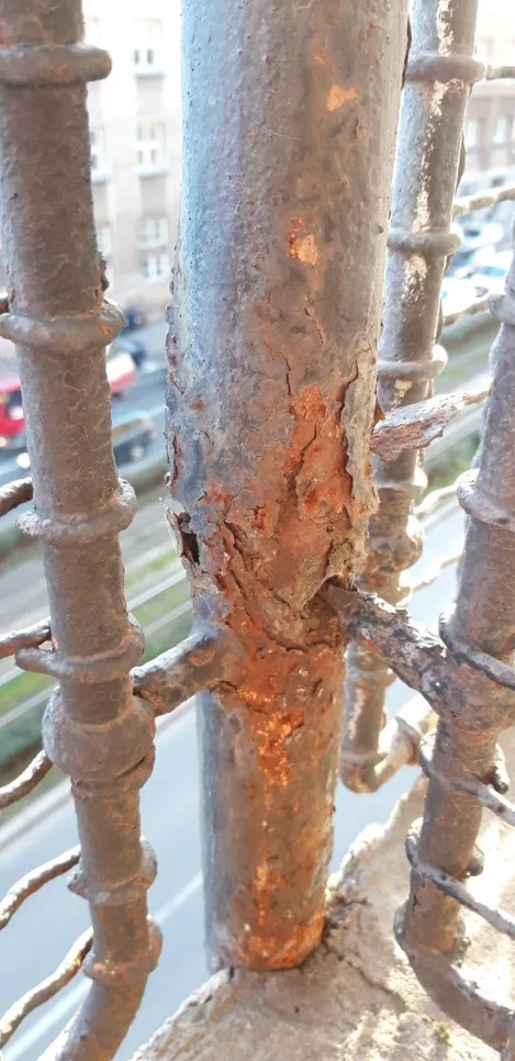Close-up of a rusty metal railing on a balcony, highlighting significant corrosion and metal decay.