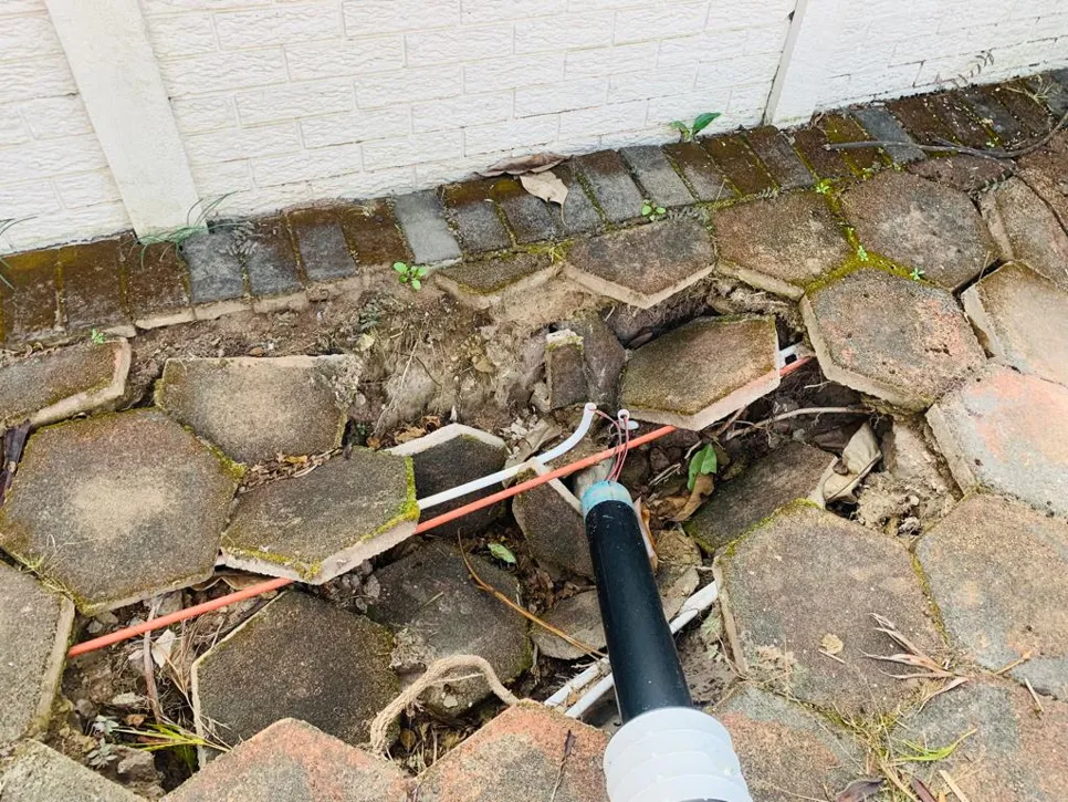 Cracked patio pavers revealing exposed electrical conduit, highlighting potential safety concerns.