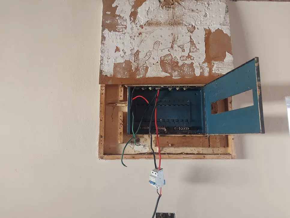 Open electrical panel with exposed wiring and peeling wall paint, indicating potential electrical hazards.