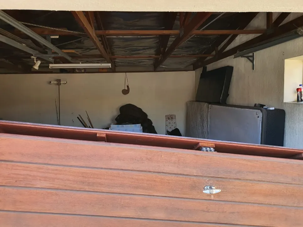 A wooden garage door is misaligned, partially open with visible interior clutter.