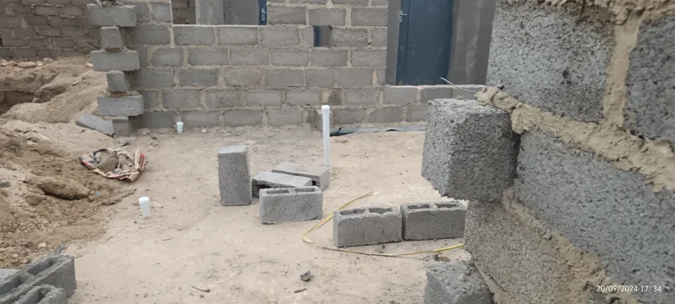 Partially built cinder block wall with scattered blocks and pipes on a construction site.