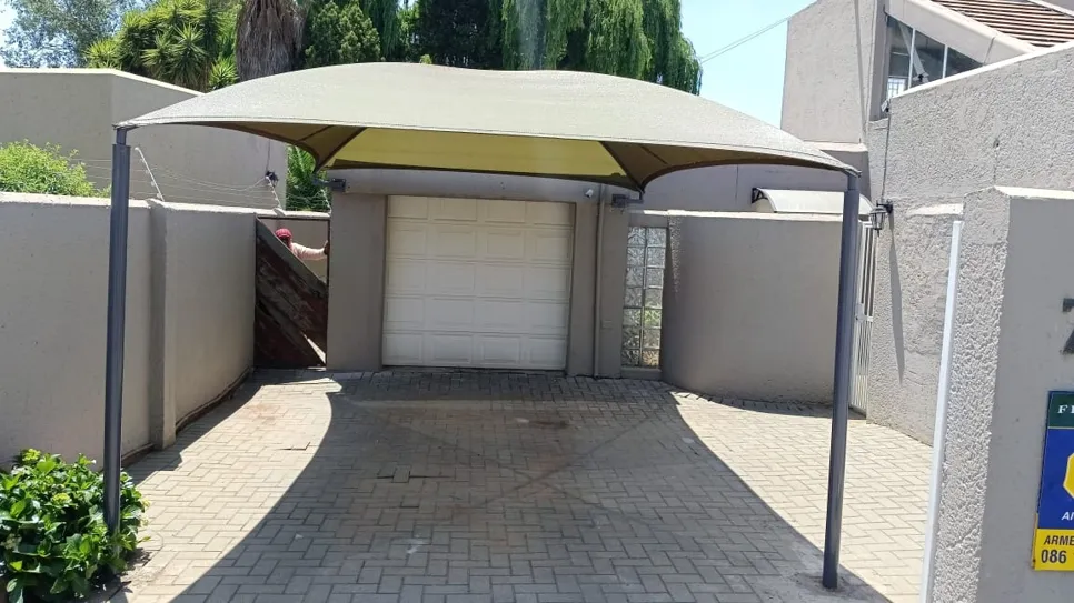 Carport with shade netting installed over a paved driveway, providing sun protection for vehicles.
