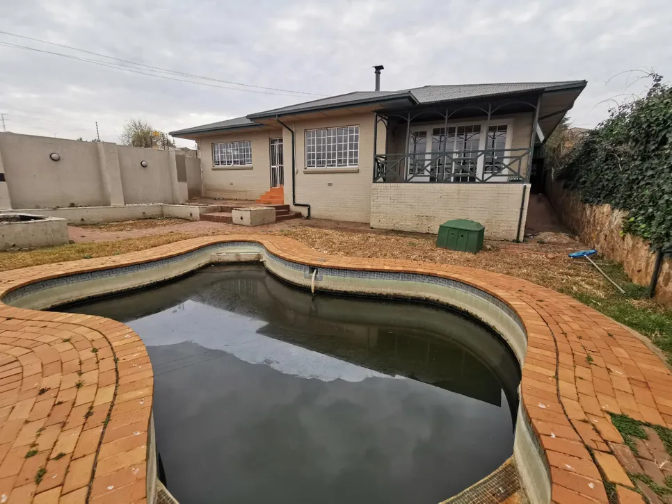 A backyard pool with murky water and surrounding brick patio, indicating neglect and potential maintenance needs.