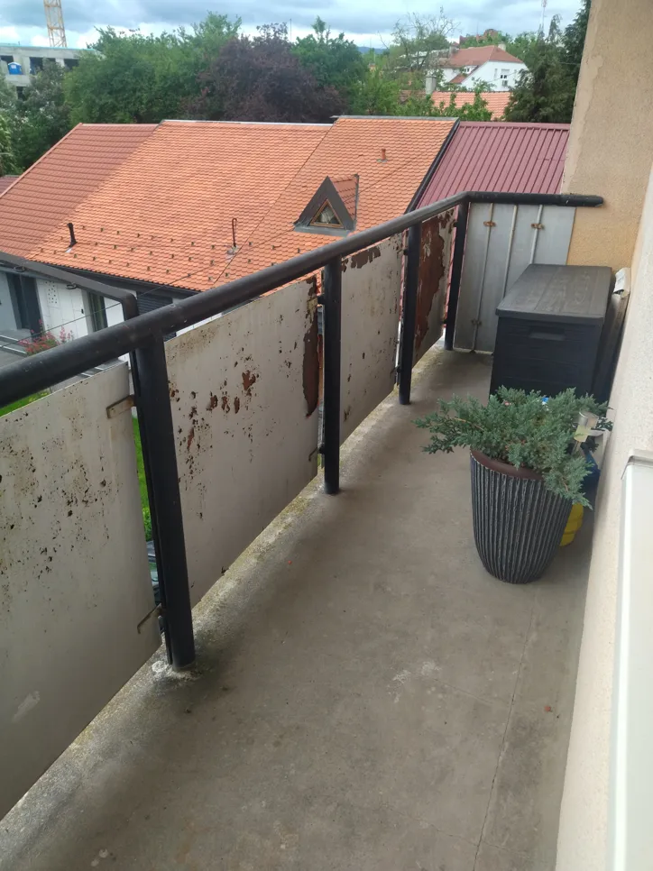 Rusty metal balcony railing with peeling paint overlooking rooftops. Outdoor wear and urban view.