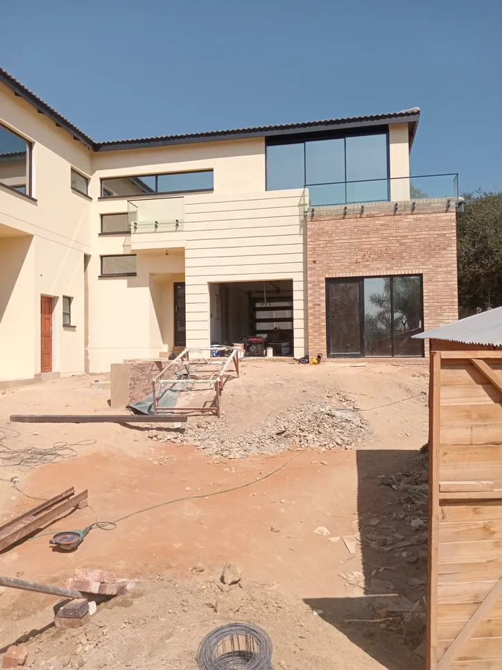 Partially constructed house exterior with unfinished landscaping, showing exposed soil and building materials.
